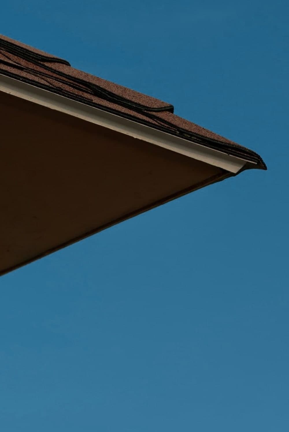 The corner of a shingled roof against a clear blue sky