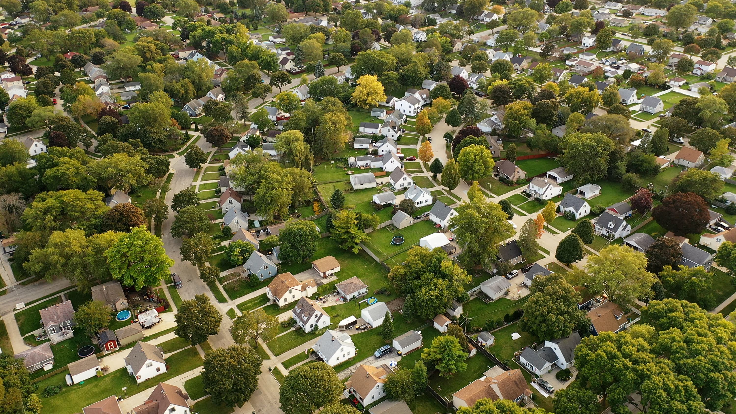 An overhead view of a suburban neighborhood, including dozens of homes with shingled roofs