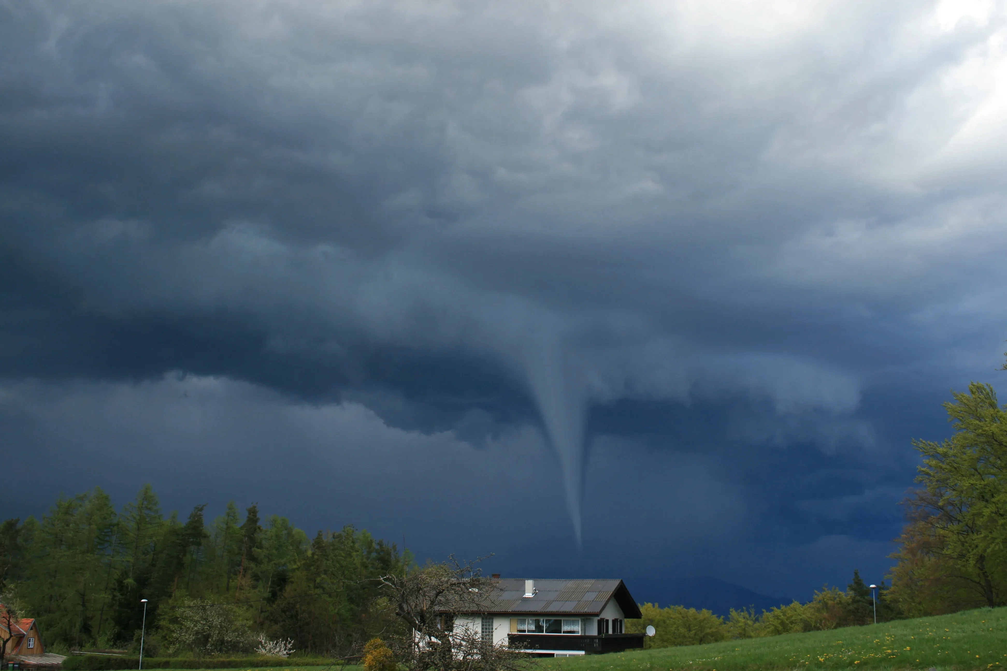 Large storm clouds and a thin tornado funnel cloud over a two-story home